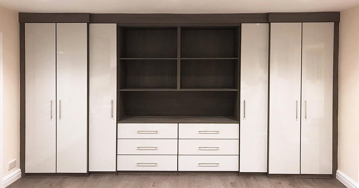 Fitted wardrobes with matching wardrobes and an open bookcase in a cream gloss and dark walnut finish with chrome handles.