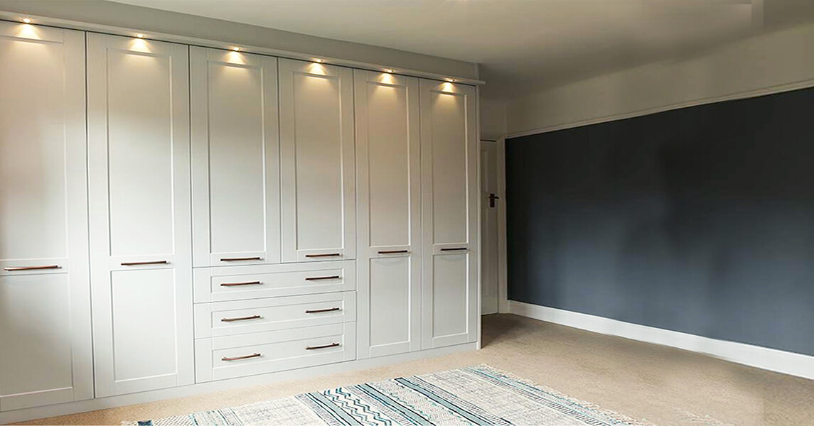 Fitted shaker-style wardrobes with built-in drawers in a matt cream finish.