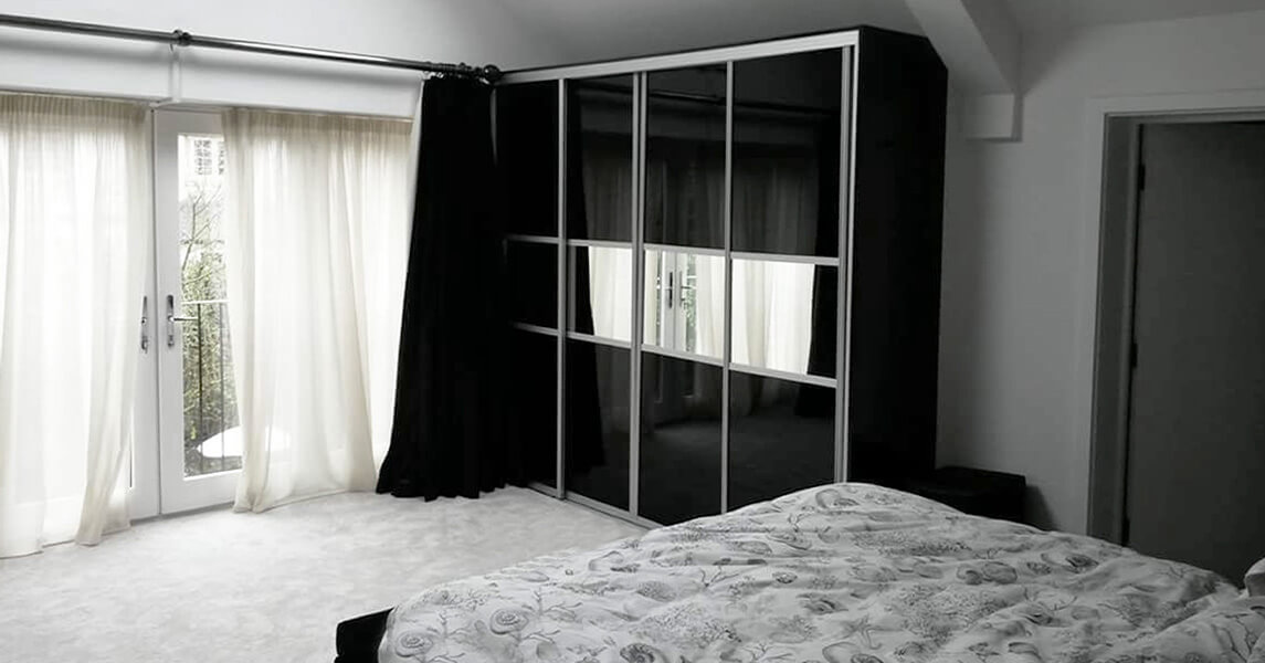 A fitted wardrobe with black gloss and mirrored sliding doors.