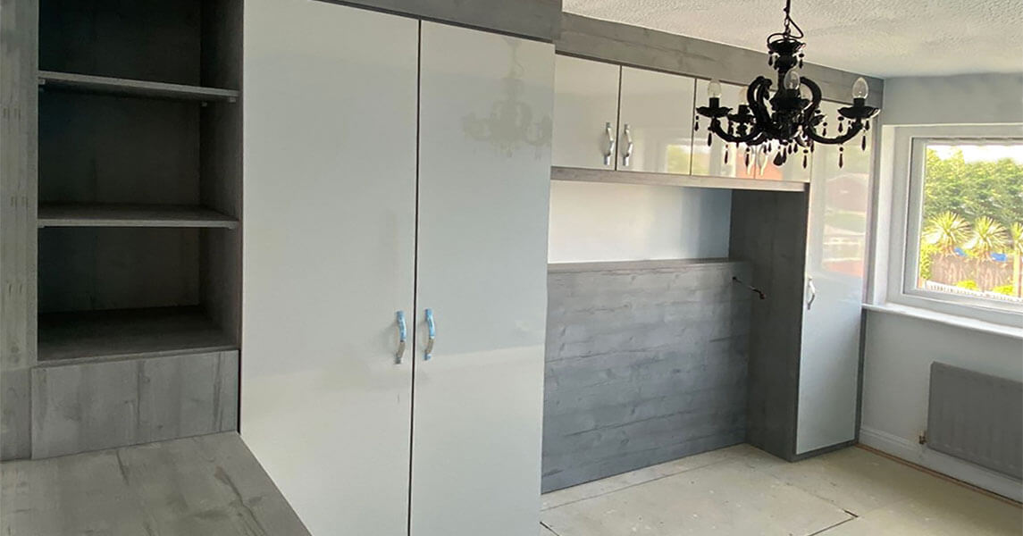 Fitted wardrobes with overhead storage and an open bookcase in a cream gloss front and a dark walnut surround.