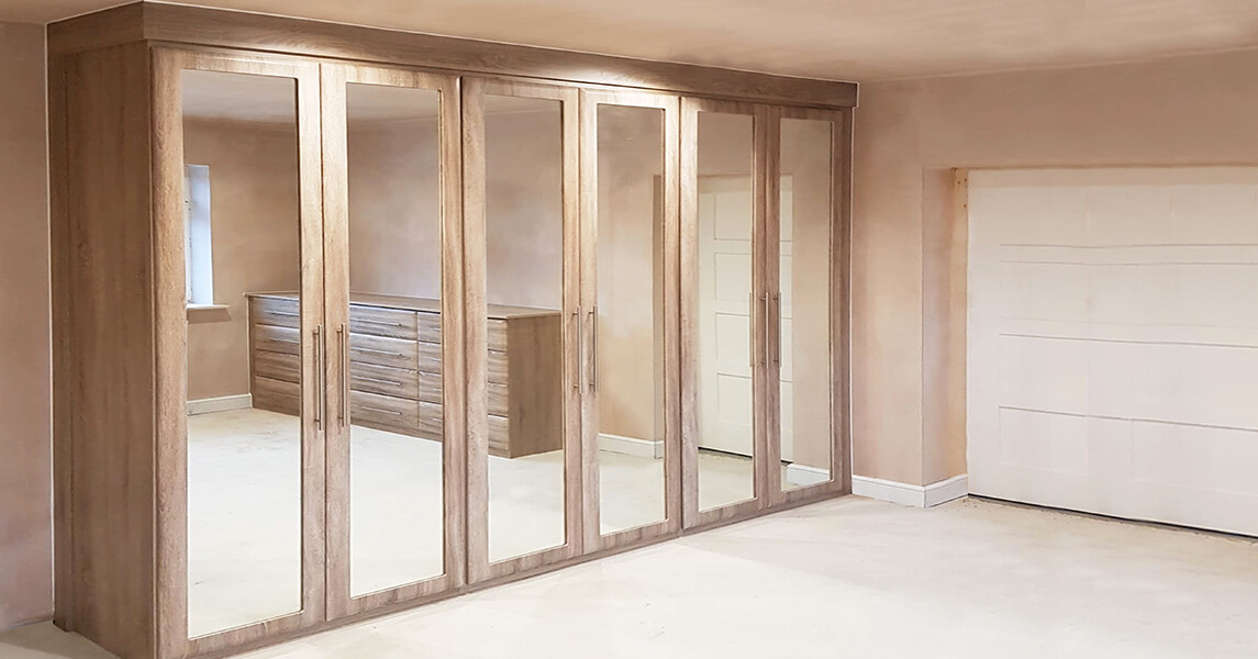 Fitted wardrobes in a mid oak finish with fitted mirrors on the doors.