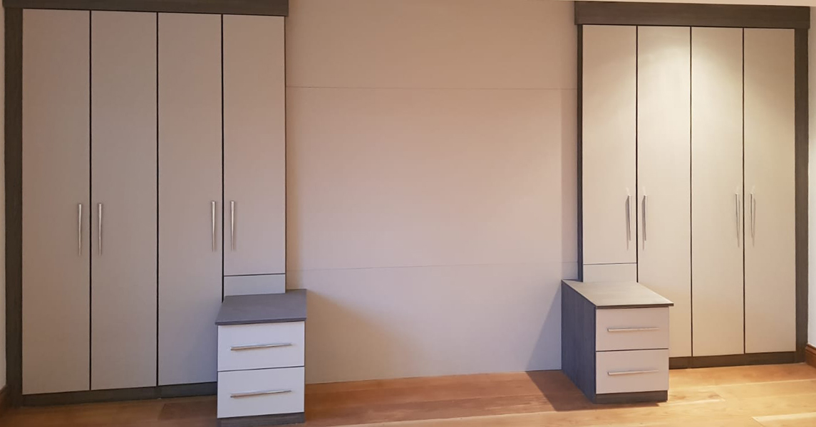 Fitted wardrobes with matching bedside tables in a cream gloss and dark walnut finish.