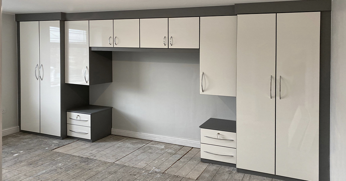 Fitted wardrobes, bedside tables, and overhead storage in cream gloss and dark wood edges.