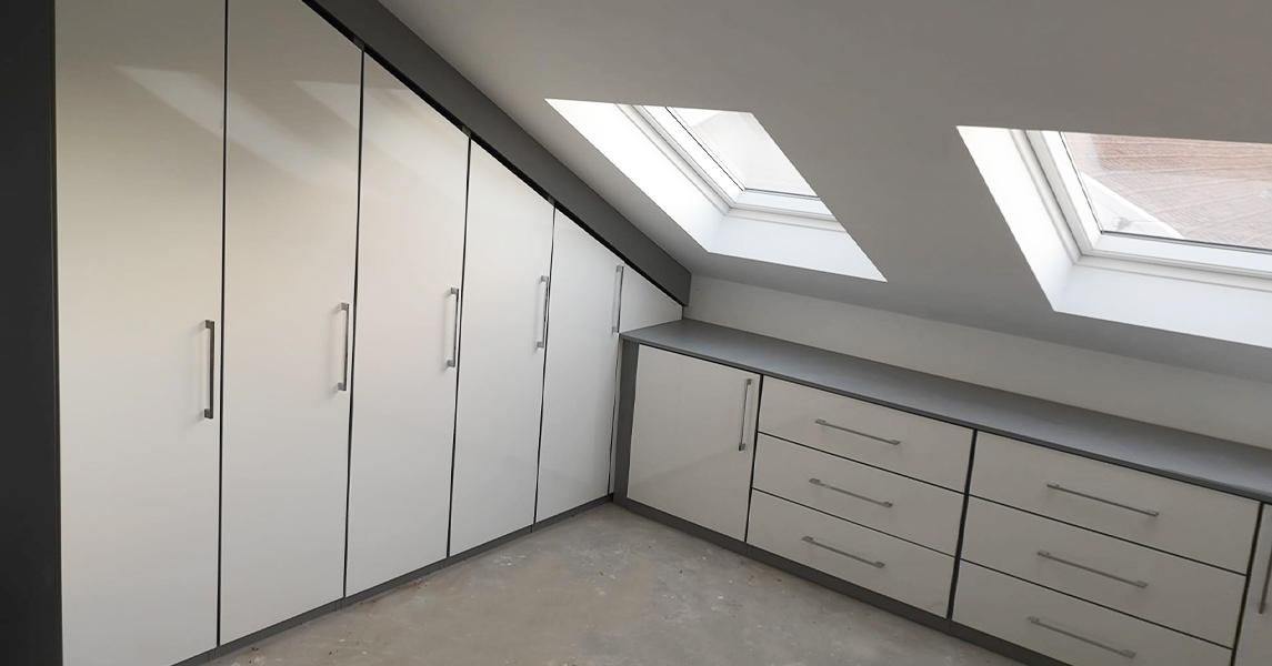 Fitted wardrobes and matching chest of drawers in an attic/loft room in a cream gloss and walnut finish.